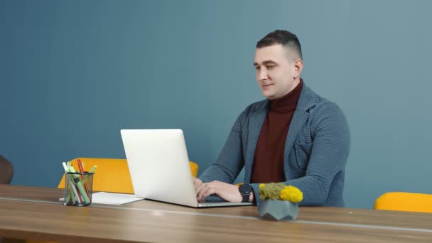 Portret pracownika biurowego patrzącego w kamerę i uśmiechającego się. Człowiek siedzący przy komputerze w biurze i pracujący. mężczyzna kaukaski biznesmen działa zdalnie za pomocą laptopa. — Wideo stockowe