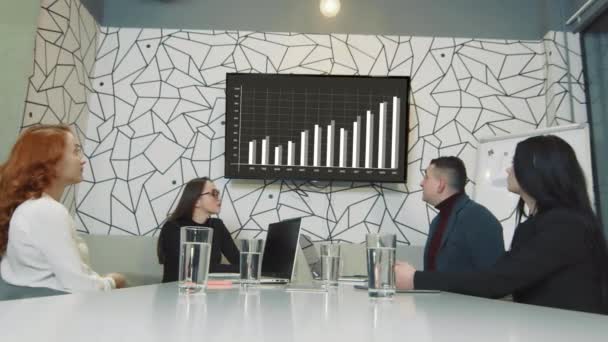 Команда умных людей в офисе обсуждают рост компании и смотрят инфографику и рост компании по телевизору. — стоковое видео