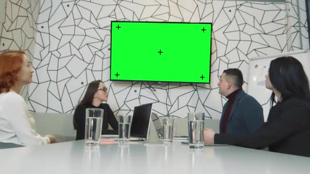 Ett team av affärsmän i ett konferensrum tittar på en bild på en TV-skärm. Chrome kaj på skärmen och vandringspunkter. Mobilkamera Affärsmän under en videokonferens — Stockvideo