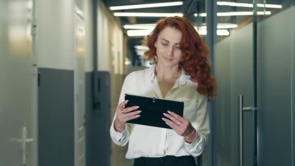 Πορτρέτο μιας επιτυχημένης επιχειρηματία με γυαλιά και μαύρα ρούχα ευρωπαϊκής εμφάνισης που στέκεται στο διάδρομο και κρατά ένα tablet. Ένας επαγγελματίας εργάζεται σε μια συσκευή αφής — Αρχείο Βίντεο