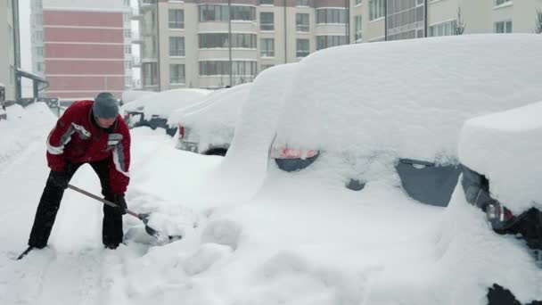 Человек очищает свою машину от снега. Снежные заносы и катаклизмы. Очистка автостоянки от снега лопатой. Человек выбрасывает снег из машины. — стоковое видео