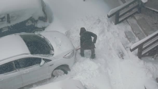 Vista superior como um homem limpa um carro estacionado perto da neve. Neve pesada. — Vídeo de Stock