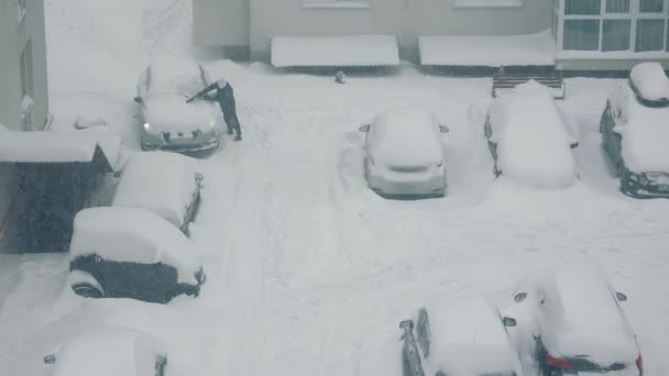 Vista superior como um homem limpa um carro estacionado perto da neve. Neve pesada. — Vídeo de Stock