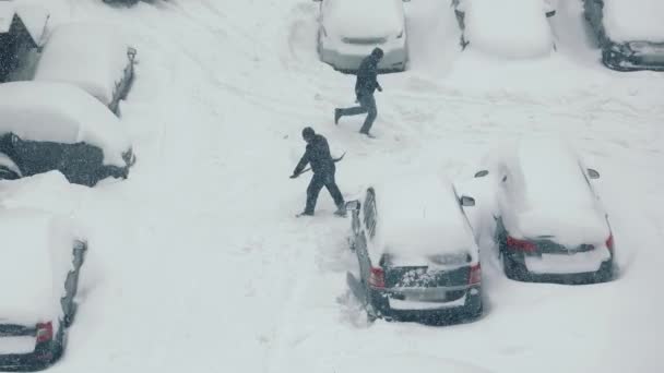 Top view som en mand rydder en bil parkeret nær sneen. Kraftigt snefald. – Stock-video