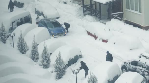 Ucrania Lviv 10.02.20201 Un coche que resbaló en la nieve. Fuertes nevadas y personas despejando sus plazas de aparcamiento en el estacionamiento de nieve. Los coches están cubiertos de nieve — Vídeo de stock