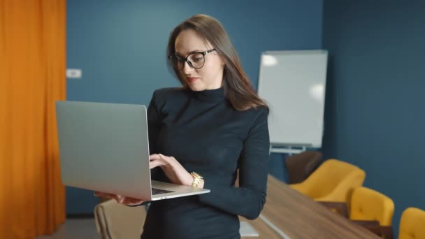 Confident and smiling business woman in glasses of Caucasian appearance working on laptop holding laptop in hands. The look of a pretty happy woman. Portrait of an office worker looking at the camera — Stock Video