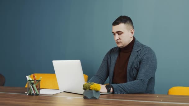 Fiatal szakállas férfi programozó kaukázusi megjelenés, ül és dolgozik egy laptopon. Egy férfi portréja, aki a kamerába néz és mosolyog. — Stock videók