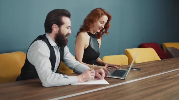 Femme tapant du texte sur un ordinateur portable dans le bureau, et à côté d'un homme avec une barbe écrivant du texte. — Video