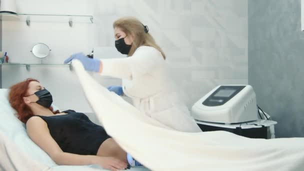 Der Arzt wickelt während eines langen Eingriffs in einem Schönheitssalon eine Decke ein. Reduktion von Cellulite und lokalisierten Fettablagerungen. Nicht-invasive Körperumformung — Stockvideo