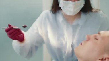 Diş hekimi, erkek bir hastanın dişlerini rutin bir şekilde muayene eder. Diş hekimi bir ayna yardımıyla dişleri inceler. Bir dişçi tarafından muayene.