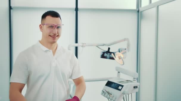 Πορτρέτο ενός νεαρού οδοντίατρου που κοιτάζει την κάμερα σε ένα οδοντιατρείο και χαμογελάει. Νέος ειδικός. — Αρχείο Βίντεο