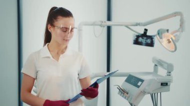 Kadın bir doktor ve geleceğin dişçisi portresi. Elinde bir dosya dolusu belge olan beyaz bir kadın dişçinin ofisinde..