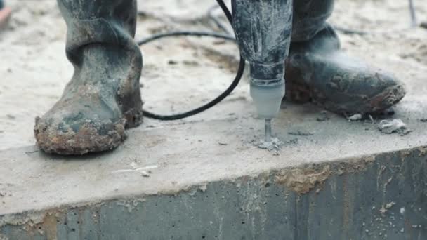Close-up van een man op een bouwplaats in vuile laarzen boor een gat in het beton. — Stockvideo