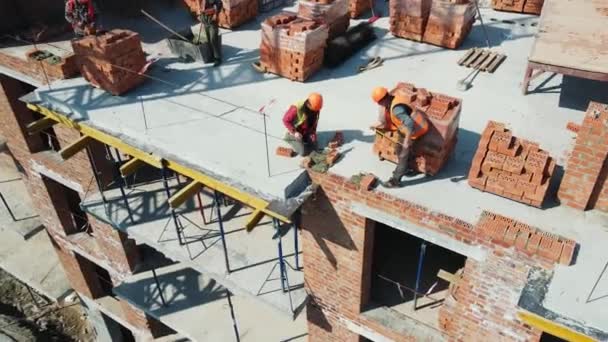 Vista aérea Construtores que trabalham na construção e colocação de tijolos. Colocação de tijolos de um edifício de vários andares — Vídeo de Stock