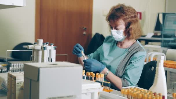 Muitos tubos de teste médicos com exames de sangue na mesa no laboratório. O profissional de saúde imprime e sinaliza rótulos para tubos de ensaio — Vídeo de Stock