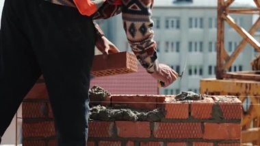 Tuğla ev inşa eden bir adama yaklaş. Güneşli bir günde şantiyeye kırmızı tuğla döşemek. Ev inşaatı bitti..