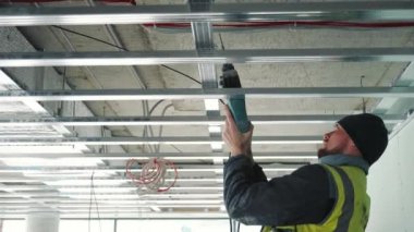 Tavana matkapla delik açan bir usta. Sahte tavanlar oluşturma.