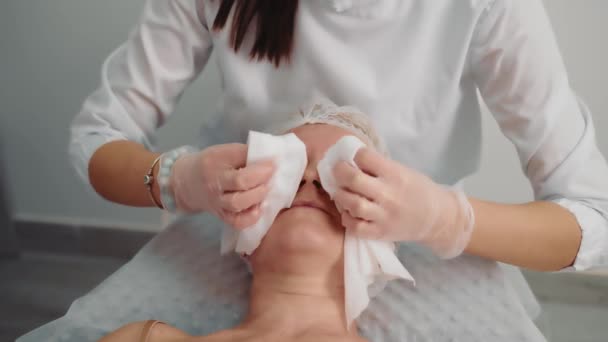 O esteticista limpa o rosto com toalhetes molhados. Desinfecção facial durante procedimentos estéticos. Close up de mulheres rosto limpo com guardanapos. — Vídeo de Stock