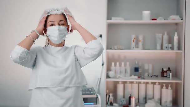 Porträtt av en kosmetolog läkare bär en skyddande medicinsk mask i en skönhetssalong. Bild av en kosmetolog under pandemin — Stockvideo