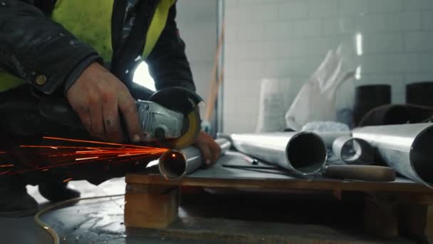 Cerrajero masculino trabajando en producción. Un hombre corta una tubería de metal con la mano sin protección. Chispas volando cortando una tubería de metal. — Vídeos de Stock