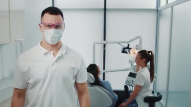 Diş kliniğindeki bir dişçinin portresi. Doktor, Kafkas uyruklu bir adam. Arka planda hasta ve doktor var..