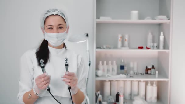 Porträtt av en kosmetolog som håller elektriska elektroder av mikroströmsterapi. Kosmetolog mikroströmsterapi. — Stockvideo