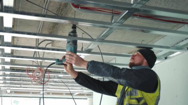 Tavana matkapla delik açan bir usta. Sahte tavanlar oluşturma.