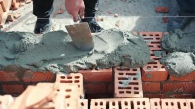 İnşaatçı, tuğla üzerine çimento çözeltisi uygular ve kırmızı tuğla evin duvarlarını inşa eder..