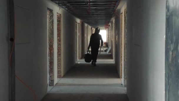 Silhueta de um trabalhador da construção civil caminhando por um corredor escuro com uma ferramenta em suas mãos — Vídeo de Stock
