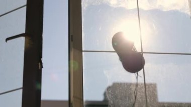 Pencereleri temizleyen bir robot. Sabah güneşinin ışınları odayı aydınlatıyor. Pencereleri silen bir robotun silüeti