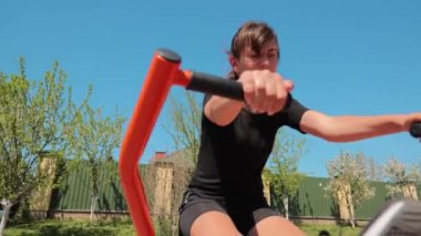 Kız güneşli bir günde sokakta spor yapmaya gider. Dışarıdaki simülatörler üzerinde alıştırmalar.