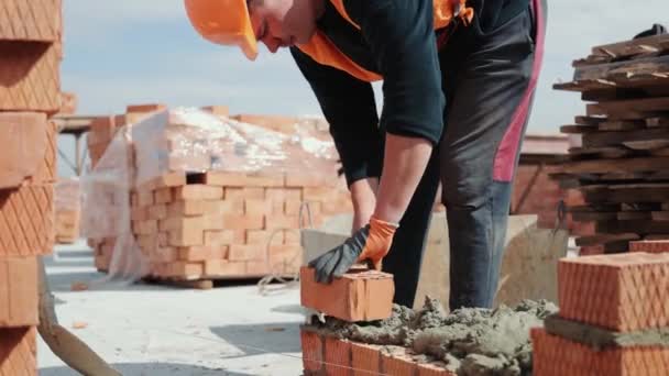 Primer plano de un hombre construyendo una casa de ladrillo. Colocación de ladrillos rojos en un sitio de construcción en un día soleado. Construcción de casas de cerca. — Vídeo de stock