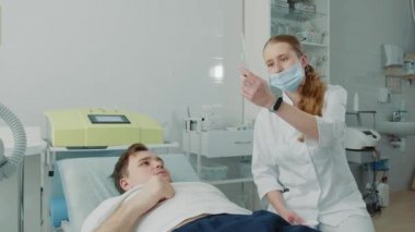 Hasta klinik koğuşundaki genç bir hemşireyle iletişim kuruyor. Hemşire annesiyle iletişim kuruyor ve elinde bir şırınga tutuyor..