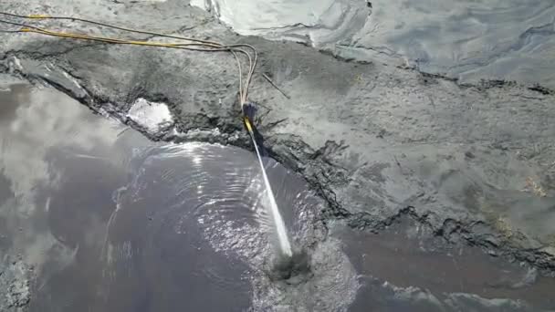 Рабочий смывает землю большим потоком воды. Ополосните почву водой высокого давления. Вода под давлением вытекает из шланга. Аллювиальные остатки сточных вод. — стоковое видео