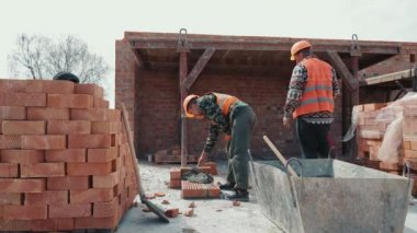 İki inşaatçı, çok katlı bir binanın inşaatına tuğla duvar örüyor..