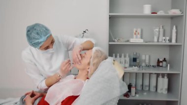 Güzellik salonunda bir kadının yüz terapisi. Kozmetik uzmanı hastaların yüzüne enjeksiyon yapıyor. Dudak büyütme prosedürü, yüzündeki kırışıklıkların azaltılması, cilt yenilenmesi.