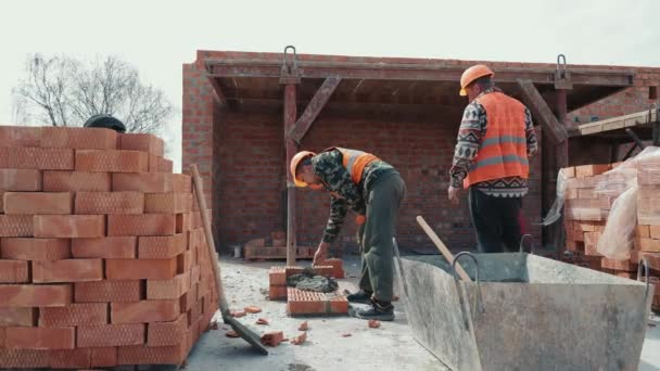 Dos constructores colocando una pared de ladrillo en la construcción de un edificio de varios pisos. — Vídeos de Stock