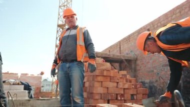 İnşaatçılar tuğla duvar örüyor. İnşaat işi. Efendiler tuğla döşeyip evin duvarını örüyorlar..
