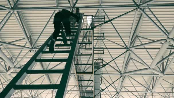 Silueta de una ingeniera subiendo una escalera de metal. Un hombre ayuda a una mujer. El hombre extiende su mano a la mujer. — Vídeos de Stock