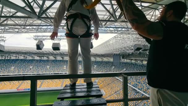 Ukraina. Lwów. 01.07.2021 r. Facet skaczący z dachu stadionu futbolowego na bungee jumping. Widok z tyłu. — Wideo stockowe