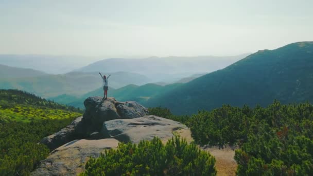 Mujer feliz excursionista en las montañas girando de pie sobre una roca con los brazos levantados. Paisaje matutino en las montañas al amanecer. Panorama de las montañas de los Cárpatos Ucranianos. — Vídeo de stock
