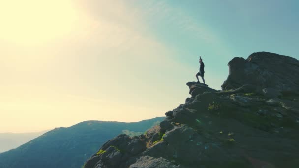 Aeria volando alrededor de un hombre de pie en la cima de una montaña levantando las manos y mirando a la distancia. Silueta de un turista sobre una roca mirando al futuro al atardecer — Vídeo de stock