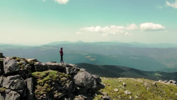 Vuelo sobre una mujer de pie en la cima de una montaña y mirando al futuro. Cima de la montaña con piedras grandes y una joven de pie sobre una piedra. — Vídeo de stock