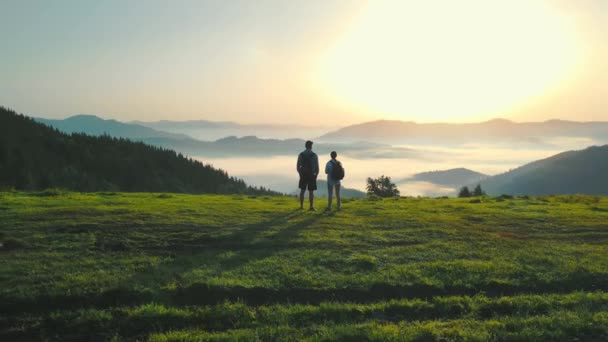 Ένας άντρας και μια γυναίκα στην κορυφή ενός βουνού συναντούν την ανατολή του ηλίου. Πρωινή ομίχλη σε μια κοιλάδα του βουνού. Όμορφο τοπίο της Ουκρανίας Καρπάθια για δύο τουρίστες. — Αρχείο Βίντεο