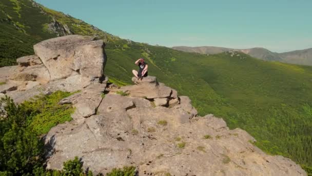 Vue aérienne Un jeune athlète masculin assis sur le bord d'une falaise, et regardant au loin. Regardant vers l'avenir. Randonneur reposant sur la montagne tout en montant au sommet. — Video