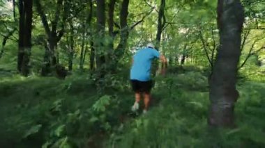 Ukrayna. Lviv. 13.07.2021 genç erkek sporcu şehir parkında çalılar arasında koşuyor. Sabah koşusu, ormanda koşmak, adam koşmak, arkadan bakmak.