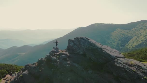 El excursionista está parado sobre una roca, mirando hacia el futuro al atardecer. Hombre atleta de pie en la cima de una montaña mirando a la distancia. Vista aérea en círculo desde la parte posterior — Vídeo de stock