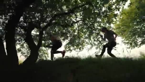 Twee meisjes rennen onder de bomen, vallende atleet terwijl ze rennen, zijaanzicht, op de achtergrond van de stad. Morgenvlucht. vallen tijdens het rennen — Stockvideo