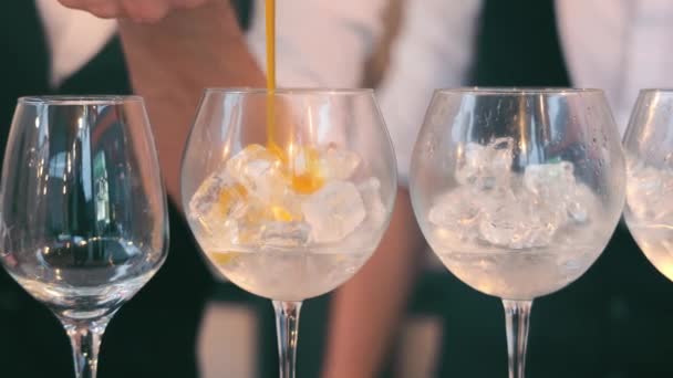 Närbild av en bartender häller apelsinlikör i ett glas med is. Göra cocktails med is. — Stockvideo