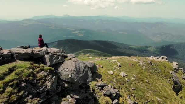 Une femme assise au sommet d'une montagne regarde au loin la beauté des montagnes des Carpates. Vue aérienne. Silhouette d'une femme assise sur une montagne rocheuse. Vue d'une jeune fille de la — Video